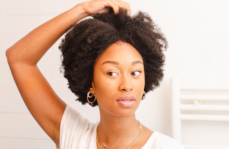 Image of Tiphanie Gueret touching her textured, coily hair.