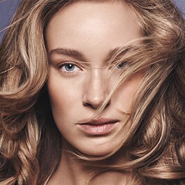 woman with long wavy hair in front of a lavender background