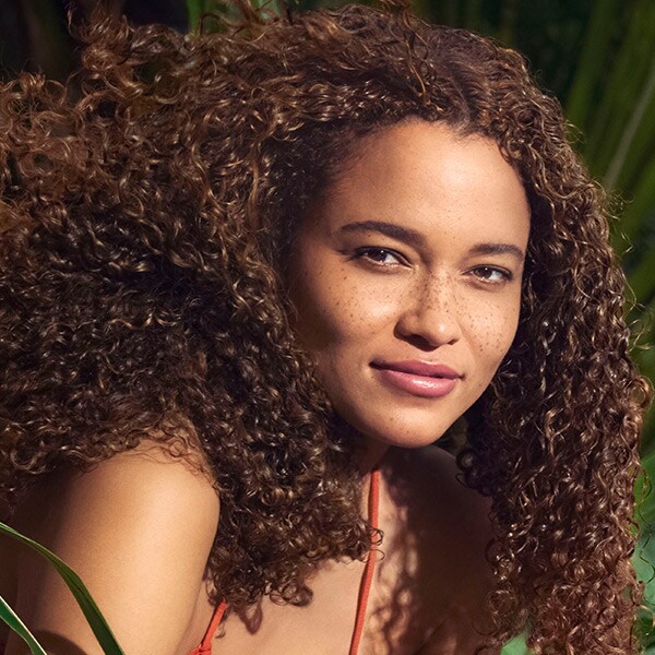 woman with long curly hair and woman with short straight hair in front of pink background